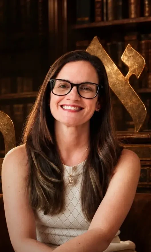 Mylena Beuttenmuller sorrindo, sentada numa biblioteca, com a letra hebraica Alef dourada ao fundo